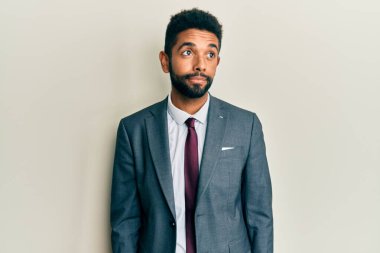 Sakallı, takım elbiseli ve kravatlı yakışıklı bir adam. Gülümsüyor ve başka tarafa bakıyor.. 