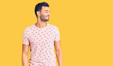 Genç, yakışıklı, günlük kıyafetler giyen, yüzünde gülümseme ve doğal bir ifadeyle yan yana bakan İspanyol bir adam. Kendinden emin gülen. 