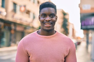 Genç Afrikalı Amerikalı adam gülümseyerek şehirde mutlu mesut duruyor..