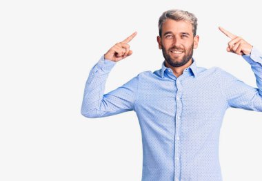 Zarif gömlek giyen yakışıklı sarışın adam gülümseyerek iki eliyle başını işaret ediyor. Harika bir fikir ya da düşünce, iyi bir hafıza. 