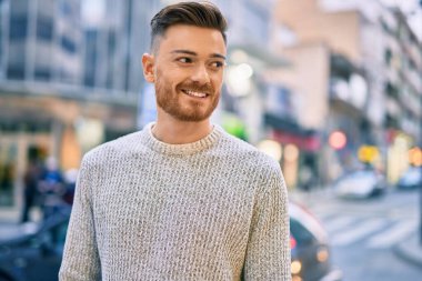 Genç beyaz adam gülümseyerek şehirde mutlu mesut duruyor..