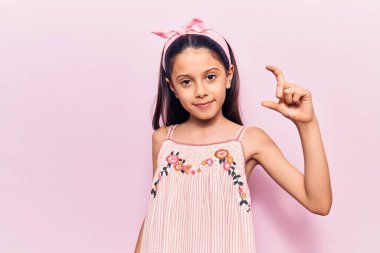 Güzel bir kız çocuğu günlük kıyafetler giyip gülümsüyor ve el hareketleriyle hareket ediyor. Küçük beden işareti yapıyor, parmaklarıyla bakıyor ve kameraya bakıyor. ölçüm kavramı. 