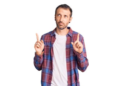 Gündelik kıyafetler giyen genç yakışıklı adam üzgün ve üzgün görünüyor, parmaklarıyla yön gösteriyor, mutsuz ve depresif. 