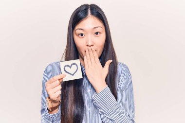 Genç, güzel bir Çinli kadın, elinde kalp şeklinde, ağzı elle kaplanmış, şok olmuş ve hata yapmaktan korkan bir hatıra tutuyor. şaşırmış ifade 