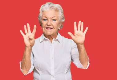 Kıdemli, gri saçlı, günlük kıyafetler giyen, dokuz numarayı gösteren ve gülümseyen, kendinden emin ve mutlu bir kadın.. 