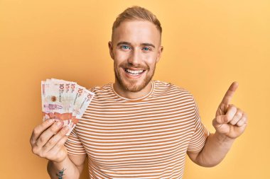 Elinde 10 Kolombiya pezosu olan genç beyaz bir adam bir fikir veya soru işareti ile gülümsüyor. 