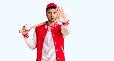 Genç İspanyol adam beyzbol sopası ve top oynuyor. Eli açık, dur işareti yapıyor. Ciddi ve kendinden emin bir ifadeyle. 