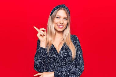 Sıradan kıyafetler giyen genç sarışın kadın gülümseyerek mutlu bir şekilde elini ve parmağını kenarda gezdiriyor. 