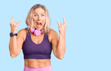 Orta yaşlı, sarışın, spor kıyafetleri giyen ve kulaklık takan çılgın bir ifadeyle el kaldırarak rock sembolü yapan bir kadın. Müzik yıldızı. ağır kavram. 