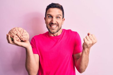 Genç yakışıklı adam beyni soyutlanmış pembe arka planda tutan gururlu, zaferi kutlayan ve kollarını kaldırarak heyecanla bekleyen özenli bir hatıra istiyor.