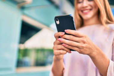 Genç beyaz kız şehirde akıllı telefon kullanarak mutlu bir şekilde gülümsüyor..