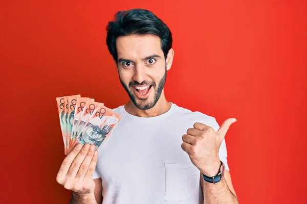 Joven Hispano Sosteniendo Dólares Australianos Apuntando Con Pulgar Hacia Costado —  Fotos de Stock