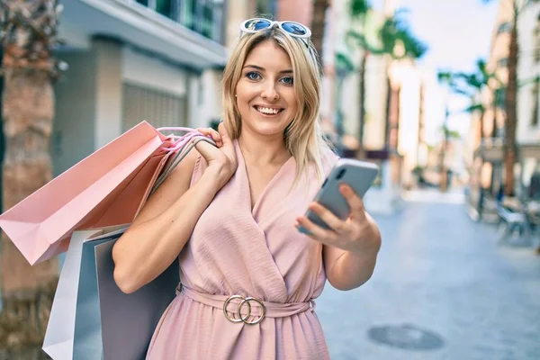 Genç Sarışın Kadın Gülümsüyor Alışveriş Torbaları Tutuyor Şehirde Akıllı Telefon — Stok fotoğraf