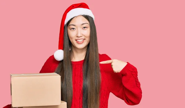 若いです中国の女性を身に着けているクリスマスの帽子保持配達パッケージを指して指に一人の自己笑顔幸せと誇り — ストック写真