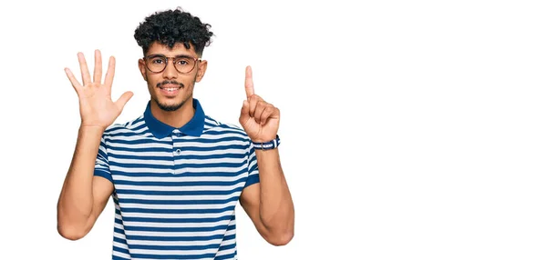 自信と幸せ笑顔ながらカジュアルな服や眼鏡を身に着けている若いアラブ人男性が表示され 指番号6で指摘します — ストック写真