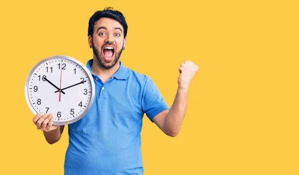 Young Hispanic Man Holding Big Clock Screaming Proud Celebrating Victory — Stock Photo, Image