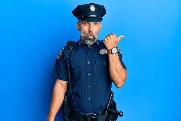 Middle age handsome man wearing police uniform surprised pointing with hand finger to the side, open mouth amazed expression.