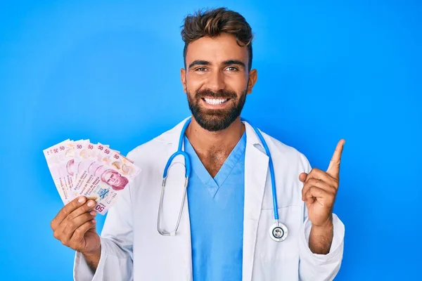 Junger Hispanischer Mann Doktoruniform Hält Mexikanische Pesos Und Lächelt Glücklich — Stockfoto