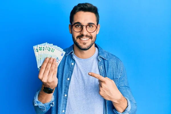 Νεαρός Ισπανός Κρατώντας Χαρτονομίσματα Των Ευρώ Χαμογελώντας Χαρούμενος Δείχνοντας Χέρι — Φωτογραφία Αρχείου