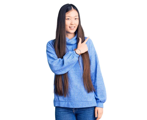 若いです美しい中国人女性身に着けていますカジュアルTurtleeckセーター陽気に笑顔で顔を指して手と指で側に幸せと自然な表現で顔 — ストック写真