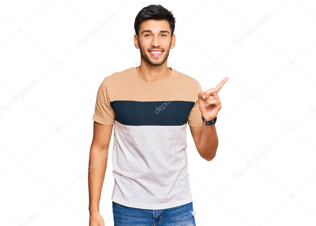 Young handsome man wearing casual clothes with a big smile on face, pointing with hand finger to the side looking at the camera. 