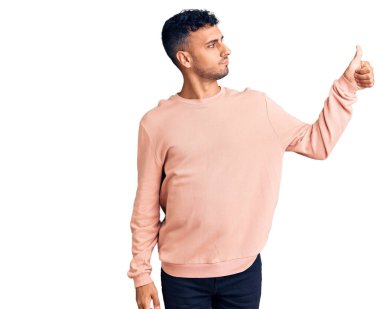 Latin asıllı, sıradan kıyafetler giyen, gururlu, gülümseyen, baş parmak kaldıran genç bir adam. 