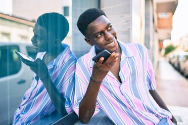Genç Afrikalı Amerikalı gülümseyen adam şehrin caddesindeki akıllı telefonda mutlu bir şekilde konuşuyor..