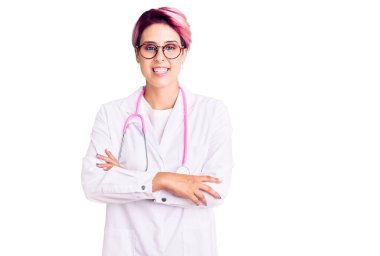 Pembe saçlı, doktor üniforması giyen, kolları çapraz gülümseyen ve kameraya bakan güzel bir kadın. pozitif kişi. 