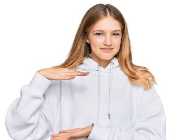 Güzel, genç, beyaz, sıradan bir kazak giyen, elleri büyük ve büyük bir işaret gösteren, ölçü sembolü olan bir kız. Kameraya bakıp gülümsüyor. ölçüm kavramı. 