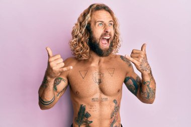 Sakallı, uzun saçlı, tişörtsüz, dövmesi olmayan, Shaka işareti yapan kızgın, sinirli ve öfkeli bir adam. Öfkeyle bağırıyor. öfke ve agresif konsept. 