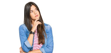 Elleri çenesinde gündelik kıyafetler giyen genç esmer kadın soru sormayı düşünüyor, düşünceli bir ifade. Düşünceli bir yüzle gülümsüyor. şüphe kavramı. 