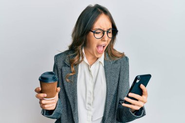 Genç esmer kadın akıllı telefon kullanıyor ve bir fincan kahve içiyor kızgın ve öfkeli çığlık atıyor öfkeyle bağırıyor. öfke ve agresif konsept. 