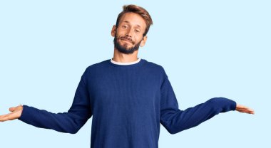 Sarışın, sakallı, sıradan bir süveter giyen, avuçlarını açıp gülümseyen, sunan, reklam yapan, karşılaştıran ve dengede duran yakışıklı bir adam. 