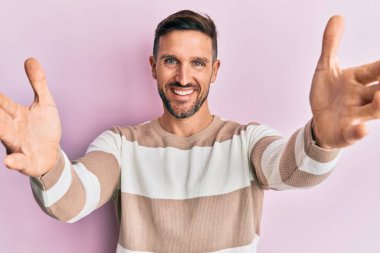 Sakallı, sıradan kıyafetler giyen yakışıklı kameraya sarılıp gülümseyen bir adam. Mutluluğu kucaklayan neşeli bir ifade.. 