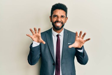 Sakallı, takım elbiseli ve kravatlı yakışıklı bir adam komik bir şekilde gülümsüyor kedi gibi pençe hareketi yapıyor, agresif ve seksi bir ifade. 