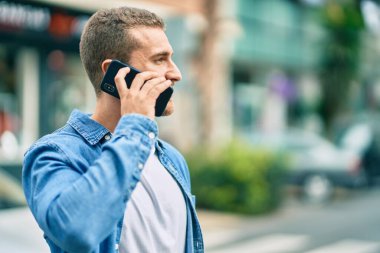 Genç beyaz adam gülümsüyor. Şehirdeki akıllı telefondan konuşuyor..