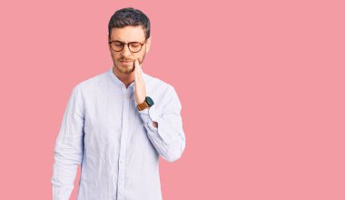 Zarif bir iş gömleği ve gözlüklü yakışıklı genç adam diş ağrısı ya da diş hastalığından dolayı acı dolu bir ifadeyle ağıza dokunuyor. dişçi 