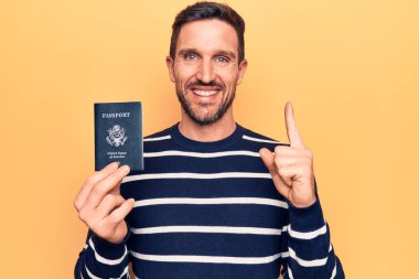 Birleşik Devletler pasaportu taşıyan genç yakışıklı turist izole edilmiş sarı arka planda bir fikir veya soru işareti ile gülümsüyor.