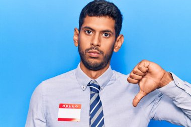 Merhaba yazılı çıkartma giyen genç latin adam benim adım kızgın yüzlü mesaj, olumsuz işaret baş parmakları aşağıda, reddedilme konsepti 