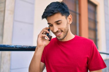 Genç Latin adam gülümsüyor ve şehirde akıllı telefondan konuşuyor..