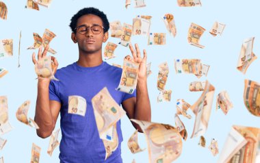 Sıradan kıyafetler giyen, gözlüklü, gülümseyen, gözleri kapalı meditasyon yaparken parmaklarıyla gülümseyen Afrikalı yakışıklı bir adam. yoga konsepti.