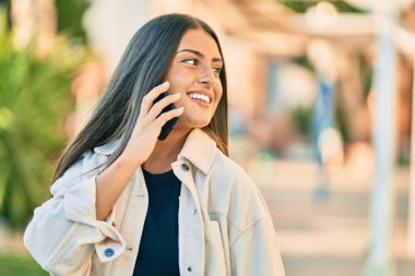 Genç İspanyol kız gülümsüyor. Parktaki akıllı telefondan konuşarak mutlu oluyor..