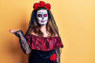 Sarı üzerine ölü kostümü giymiş genç bir kadın. Gülümseyen, elinde avucuyla kameraya bakan ve gülümseyen.. 