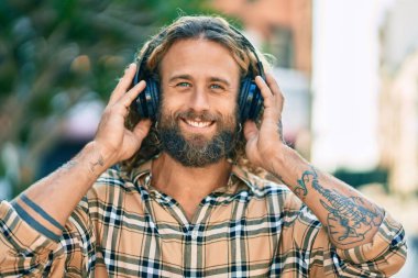 Parkta kulaklık takıp gülümseyen beyaz bir genç..