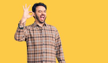 Gündelik kıyafetler giyen genç İspanyol adam gülümsüyor. El ve parmaklarıyla 