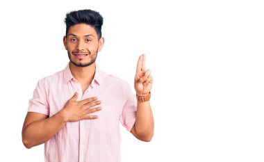 Yakışıklı Latin Amerikalı rahat bir yaz gömleği giyen gülümseyen, elleri göğsünde ve parmakları havada küfür eden, sadakat yemini eden 