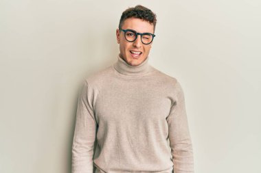 Balıkçı yaka kazak giyen İspanyol genç adam kameraya seksi bir ifadeyle bakıyor, neşeli ve mutlu bir yüzle.. 