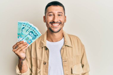 50 Yuan 'lık Çin banknotları tutan yakışıklı bir adam. Pozitif ve mutlu görünüyor. Kendine güvenen bir gülümsemeyle dişlerini gösteriyor. 