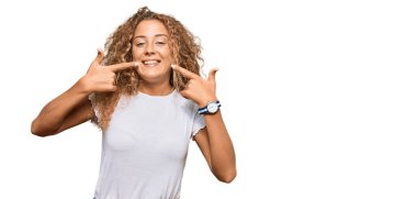 Güzel beyaz tişört giyen, neşeli gülümseyen, parmaklarıyla ve ağzıyla işaret eden beyaz kız. diş sağlığı kavramı. 