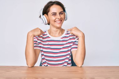 Masada oturan, kulaklık takan, kendine güvenen, gülümseyen, kendini gururlu ve mutlu gösteren genç İspanyol kadın.. 